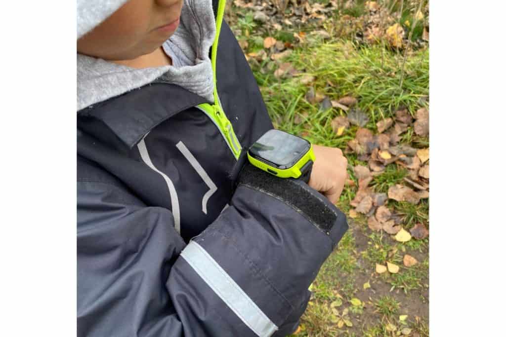 Barn med grønn og svart GPS-klokke på armen, ute i skogen