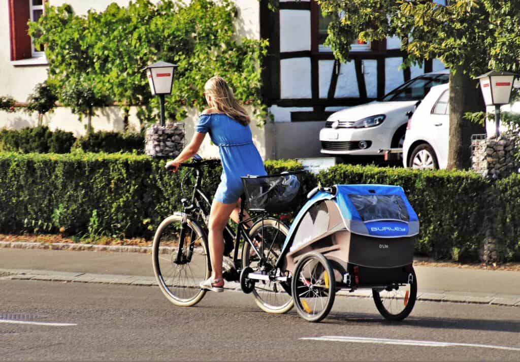 Kvinne sykler med sykkelvogn på veien