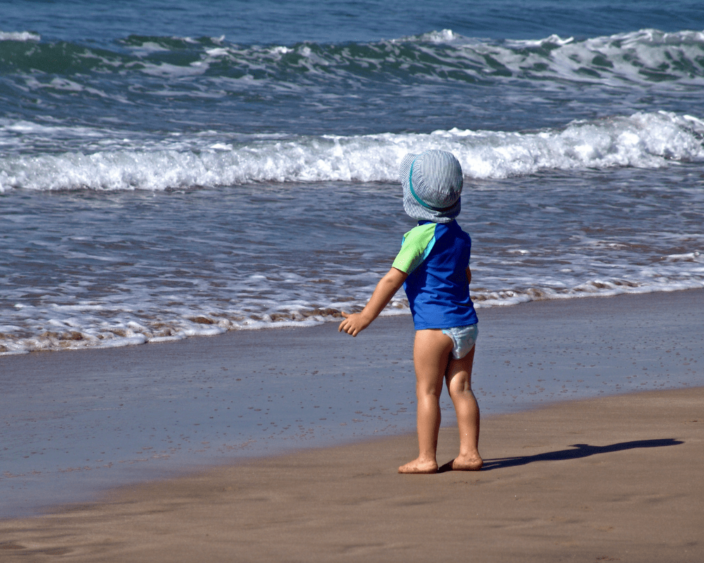 Barn med UV-klær på stranden