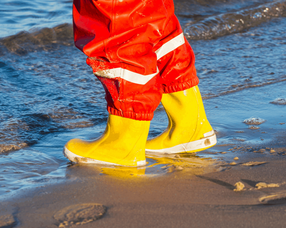 Barn med gule foret gummistøvler går langs strandlinjen