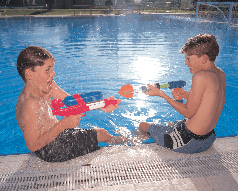 To barn ved et basseng sprøyter vann på hverandre med vannpistoler