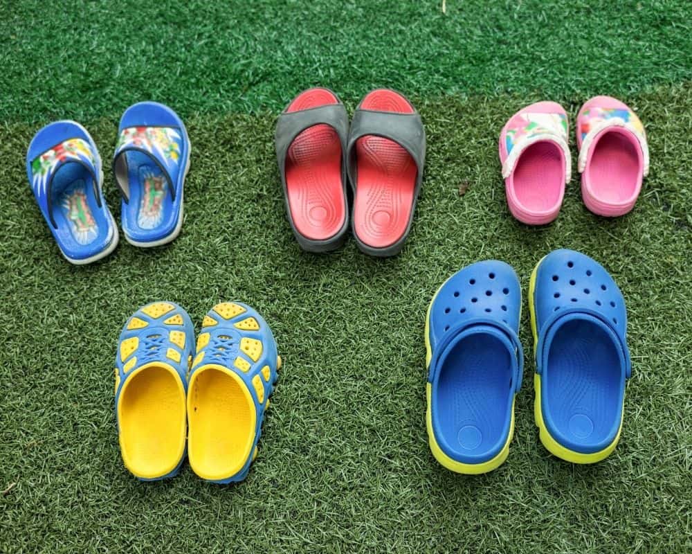 Fem fargerike sandaler for barn er stilt opp på plenen