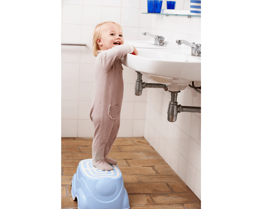 Barn rekker opp til vasken ved hjelp av skammel