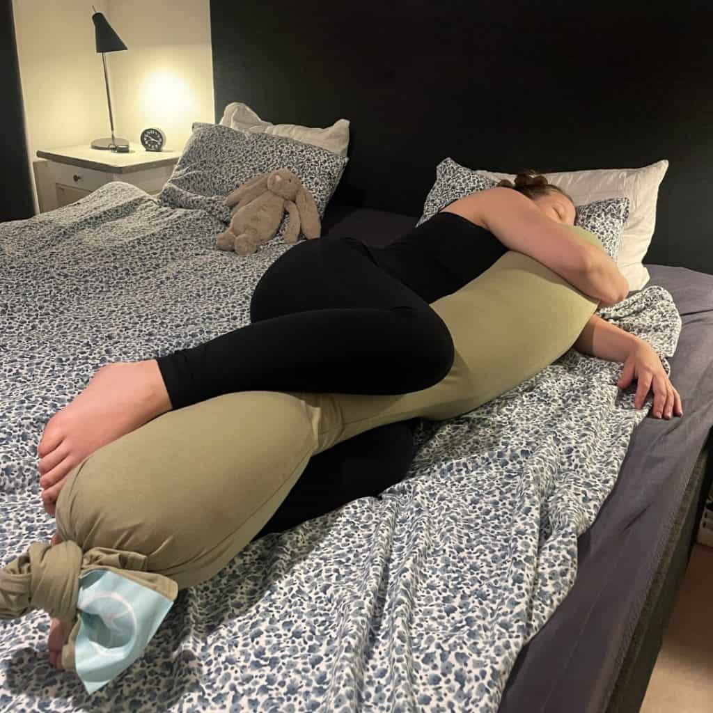 Kvinne ligger og klemmer Najell graviditetspute i sengen
